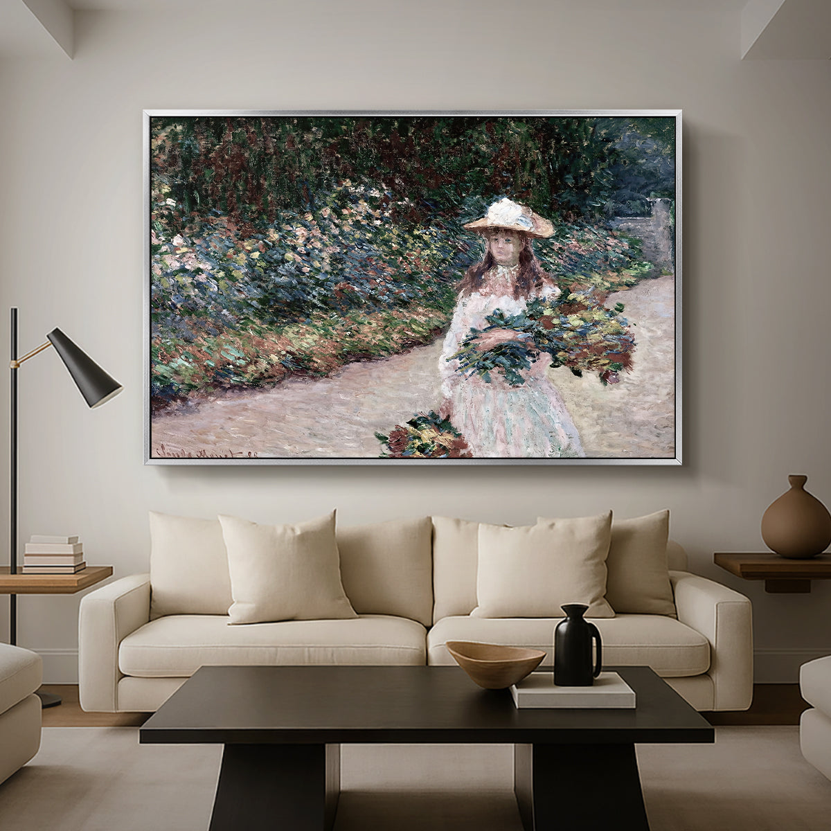 Young Girl in the Garden at Giverny, 1888 by Claude Monet as a silver floater framed canvas featuring a young girl seated in lush garden surrounded by blooming flowers, displayed above a sofa in a modern living room.