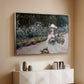Silver floater framed canvas of Young Girl in the Garden at Giverny, 1888 by Claude Monet, featuring an impressionist garden scene with child among greenery and blossoms above a console cabinet in a minimalist entryway.