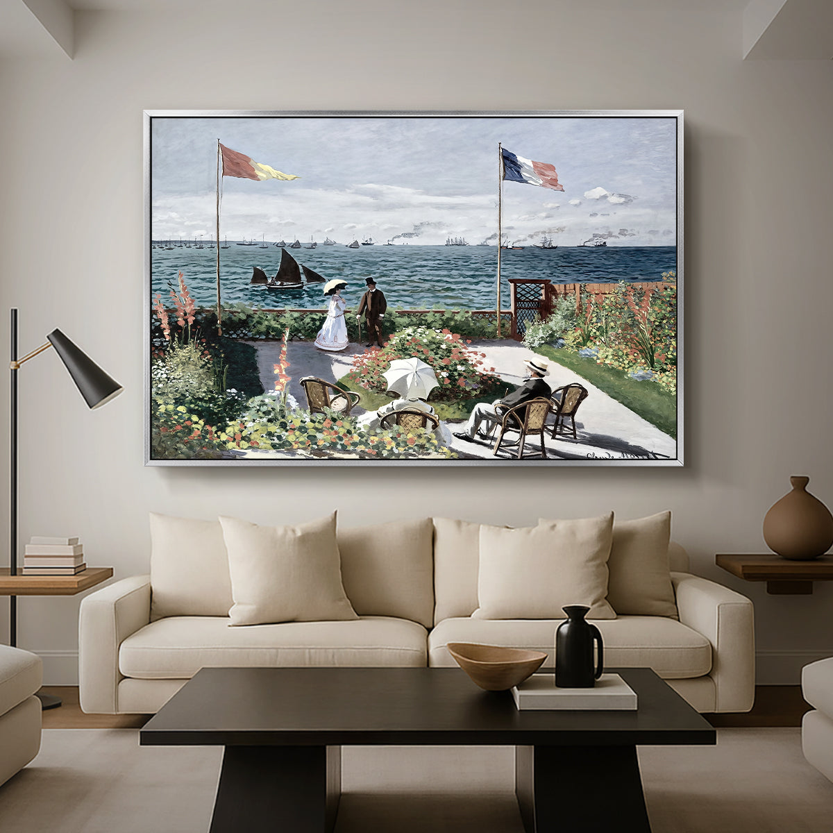 Garden at Sainte-Adresse, 1867 by Claude Monet as a silver floater framed canvas featuring a seaside garden with flowers, flags, and figures overlooking the water, displayed above a sofa in a modern living room.