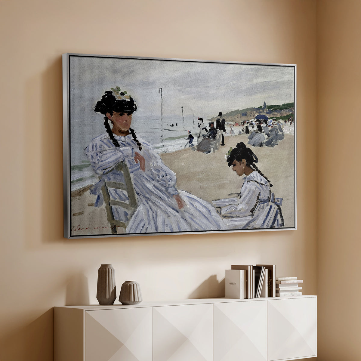 Silver floater framed canvas of On the Beach at Trouville, 1870 by Claude Monet, featuring an impressionist seaside scene with women in dresses and hats above a console cabinet in a minimalist entryway.