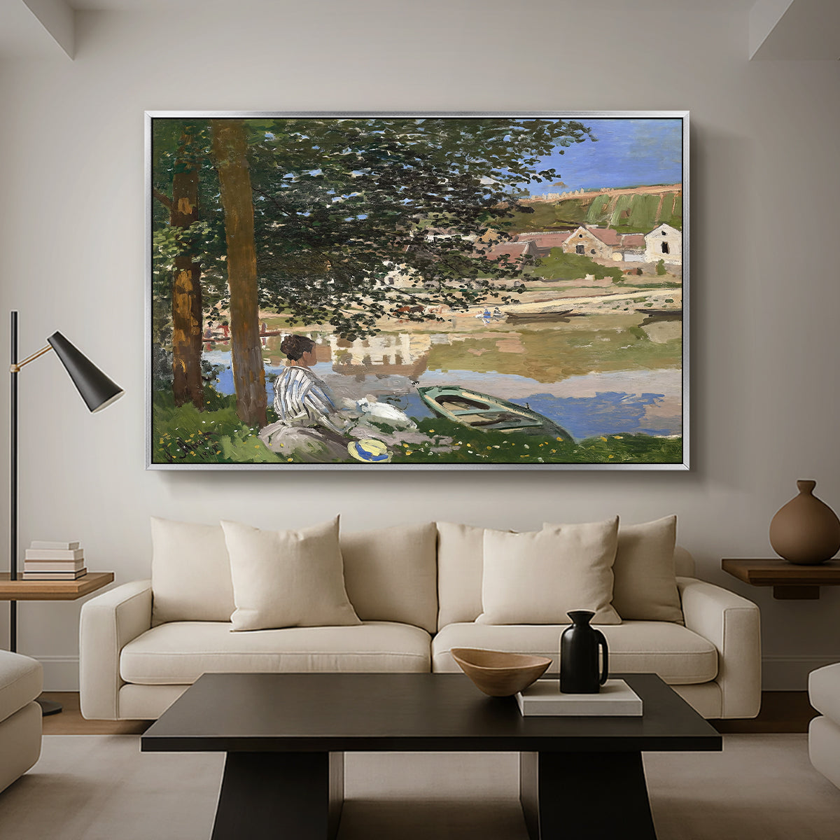 On the Bank of the Seine, Bennecourt, 1868 by Claude Monet as a silver floater framed canvas featuring a woman and child seated along riverbank beneath trees in soft daylight, displayed above a sofa in a modern living room.
