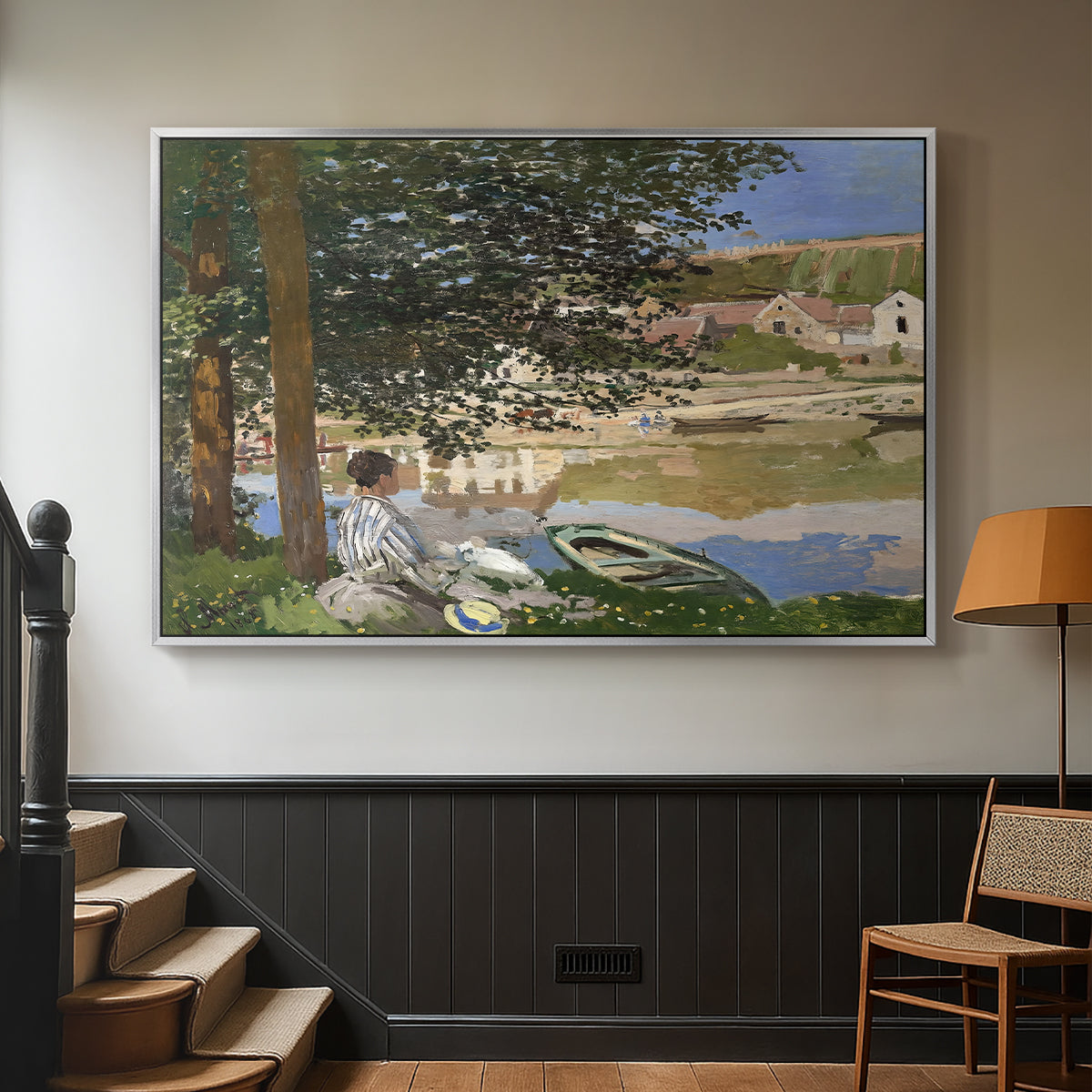 Silver floater framed canvas featuring a quiet outdoor setting with figures near river under foliage, displayed in a hallway near a staircase.