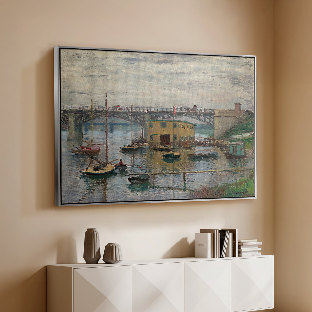 Silver floater framed canvas of Bridge at Argenteuil on a Gray Day, c. 1876 by Claude Monet, featuring an impressionist riverscape with overcast atmosphere and soft tones above a console cabinet in a minimalist entryway.