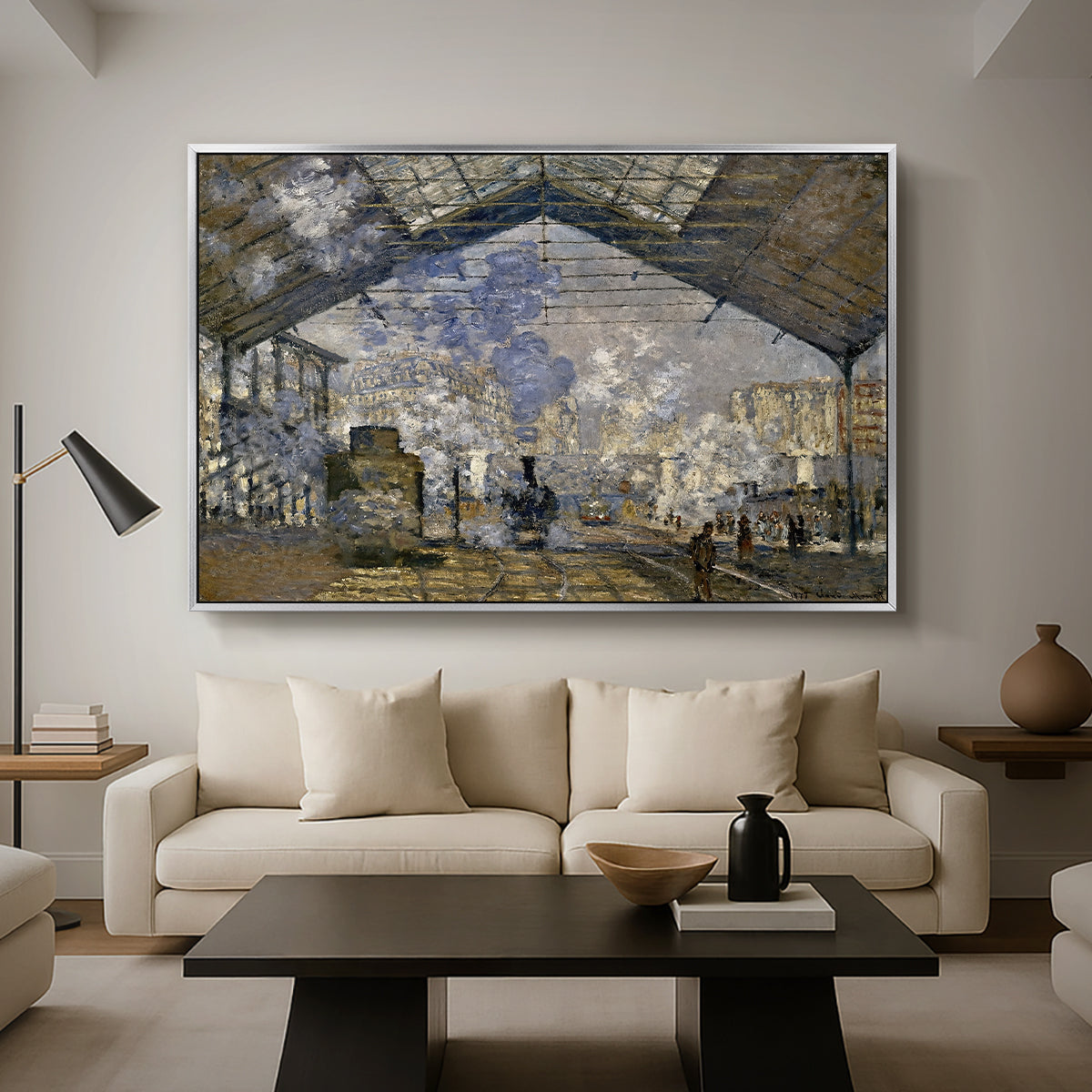 The Gare Saint-Lazare, 1877 by Claude Monet as a silver floater framed canvas featuring a train station interior filled with steam and locomotives under iron structure, displayed above a sofa in a modern living room.