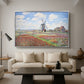 Tulip Fields with the Rijnsburg Windmill, 1886 by Claude Monet as a silver floater framed canvas featuring colorful rows of tulip fields leading toward distant windmill, displayed above a sofa in a modern living room.