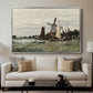 Windmill at Zaandam, 1871 by Claude Monet displayed in a silver floater framed canvas above a sofa in a clean living room.