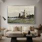 Windmill at Zaandam, 1871 by Claude Monet as a silver floater framed canvas featuring a single windmill beside water with surrounding buildings and sky, displayed above a sofa in a modern living room.