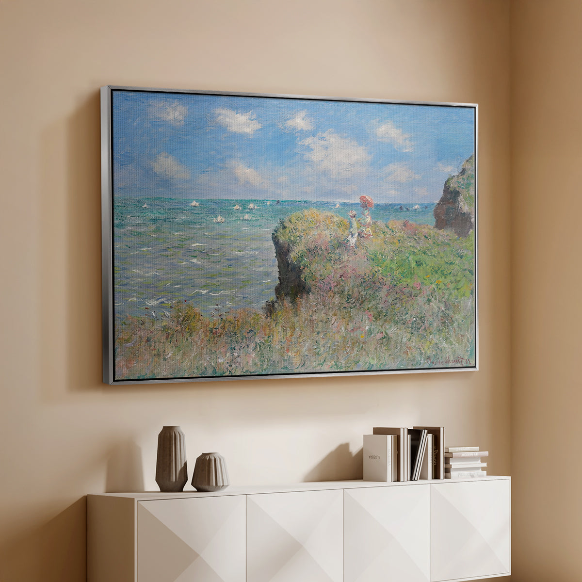 Silver floater framed canvas of The Cliff Walk at Pourville, 1882 by Claude Monet, featuring an impressionist seaside landscape with people strolling above water above a console cabinet in a minimalist entryway.
