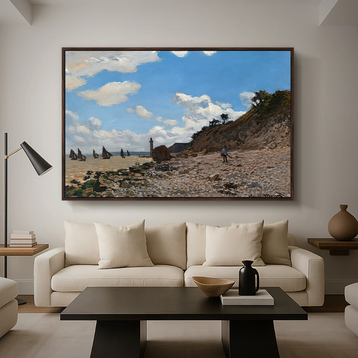The Beach at Honfleur, 1864 by Claude Monet as a walnut floater framed canvas featuring a coastal beach scene with figures gathered along shoreline and boats nearby, displayed above a sofa in a modern living room.