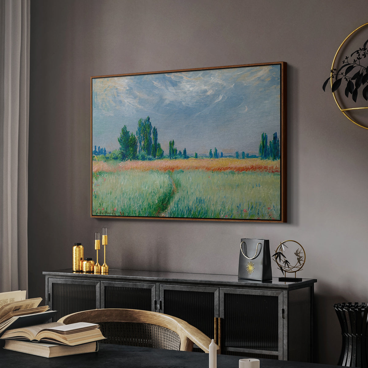 The Wheat Field (Champ de Blé), 1881 by Claude Monet in a walnut floater framed canvas featuring an agricultural landscape with tall wheat and distant horizon, displayed above a desk in a dark home office interior.