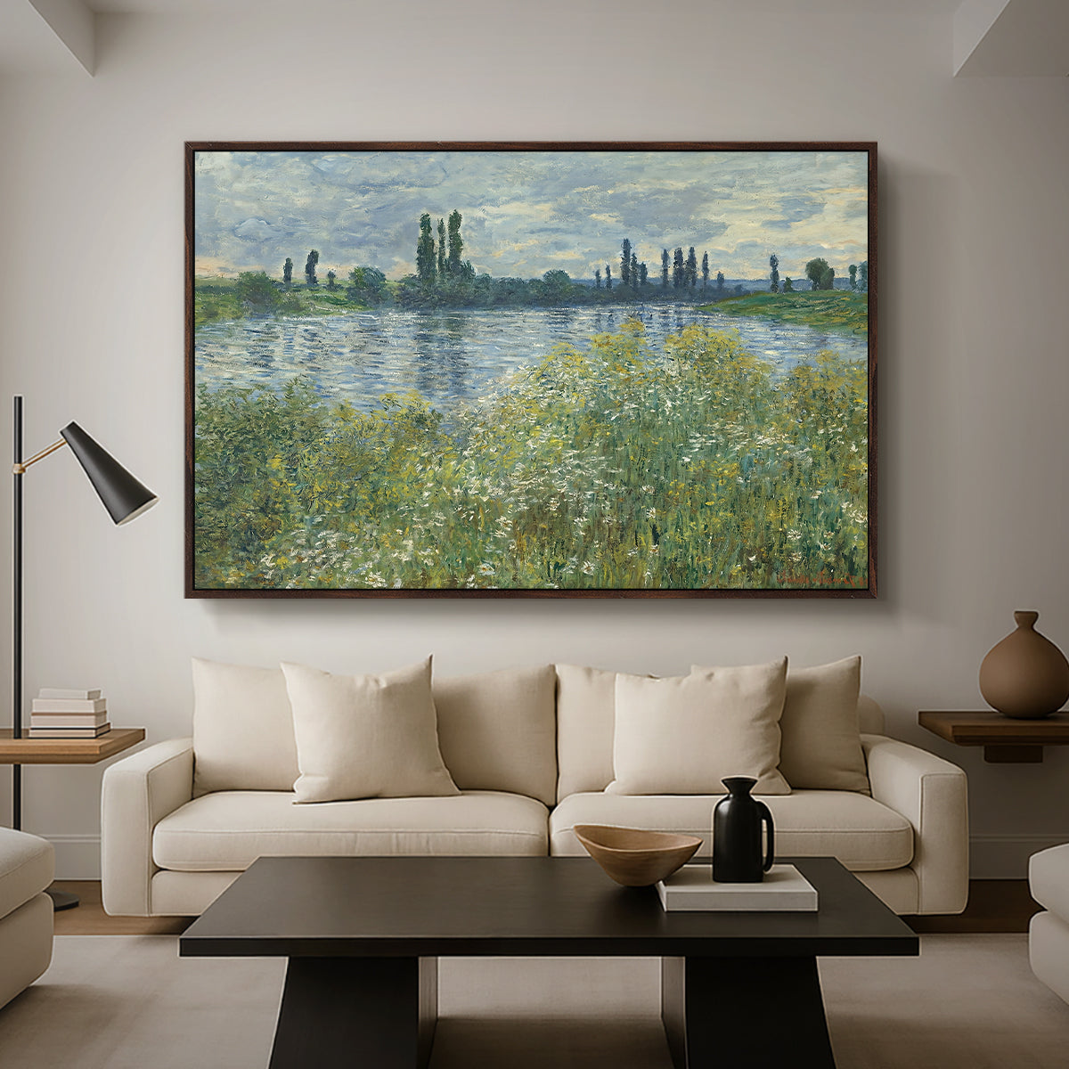 Banks of the Seine, Vétheuil, 1880 by Claude Monet as a walnut floater framed canvas featuring a riverbank landscape with water, trees, and distant village buildings, displayed above a sofa in a modern living room.