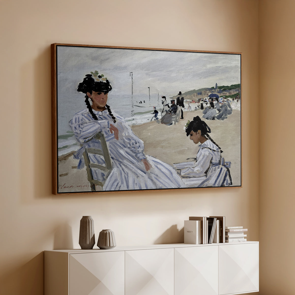 Walnut floater framed canvas of On the Beach at Trouville, 1870 by Claude Monet, featuring an impressionist seaside scene with women in dresses and hats above a console cabinet in a minimalist entryway.