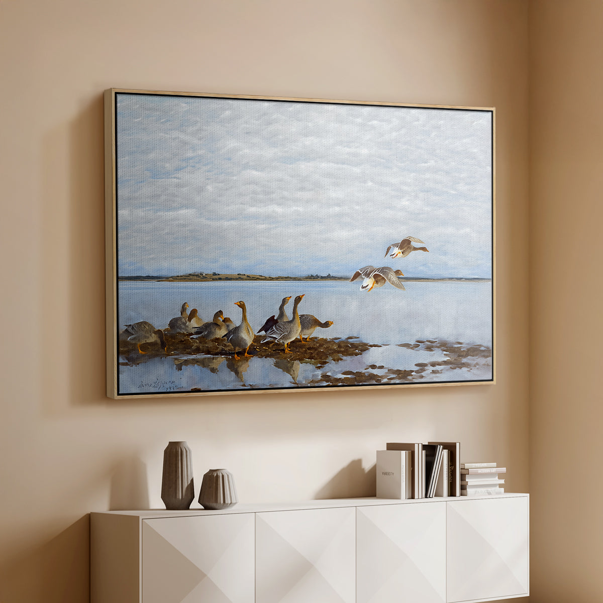 Natural wood floater framed canvas of Greylag Geese (Grågäss), 1922 by Bruno Liljefors, featuring birds standing and resting along shoreline with soft grass and water above a console cabinet in a minimalist entryway.