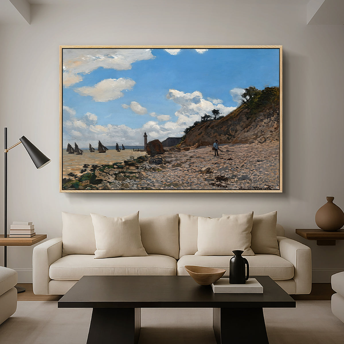 The Beach at Honfleur, 1864 by Claude Monet as a natural wood floater framed canvas featuring a coastal beach scene with figures gathered along shoreline and boats nearby, displayed above a sofa in a modern living room.