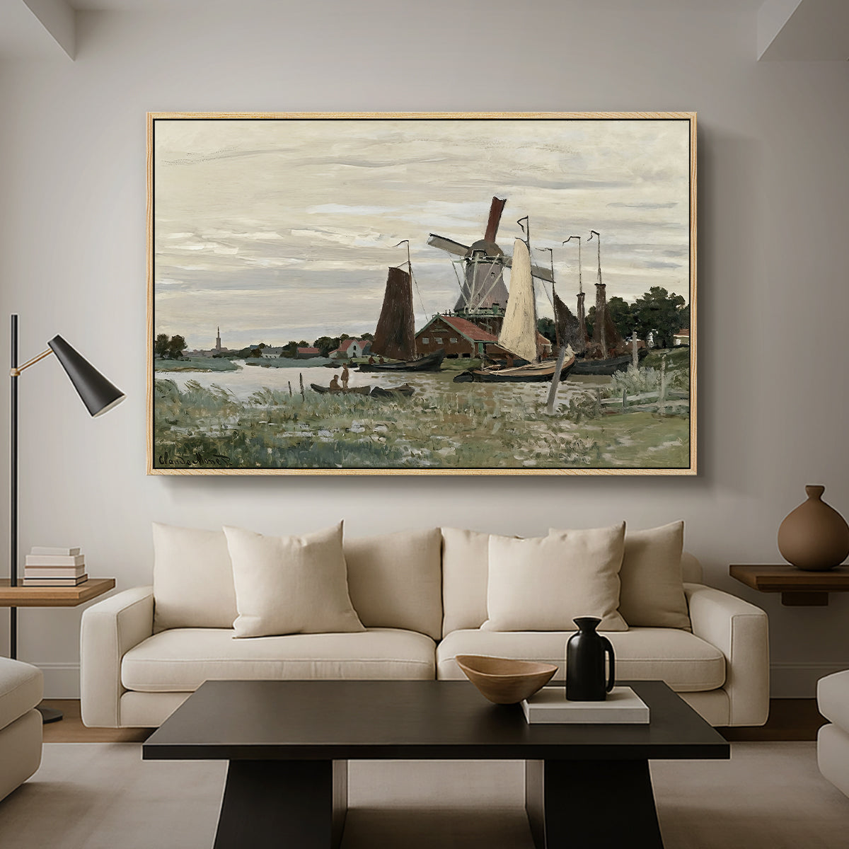 Windmill at Zaandam, 1871 by Claude Monet as a natural wood floater framed canvas featuring a single windmill beside water with surrounding buildings and sky, displayed above a sofa in a modern living room.