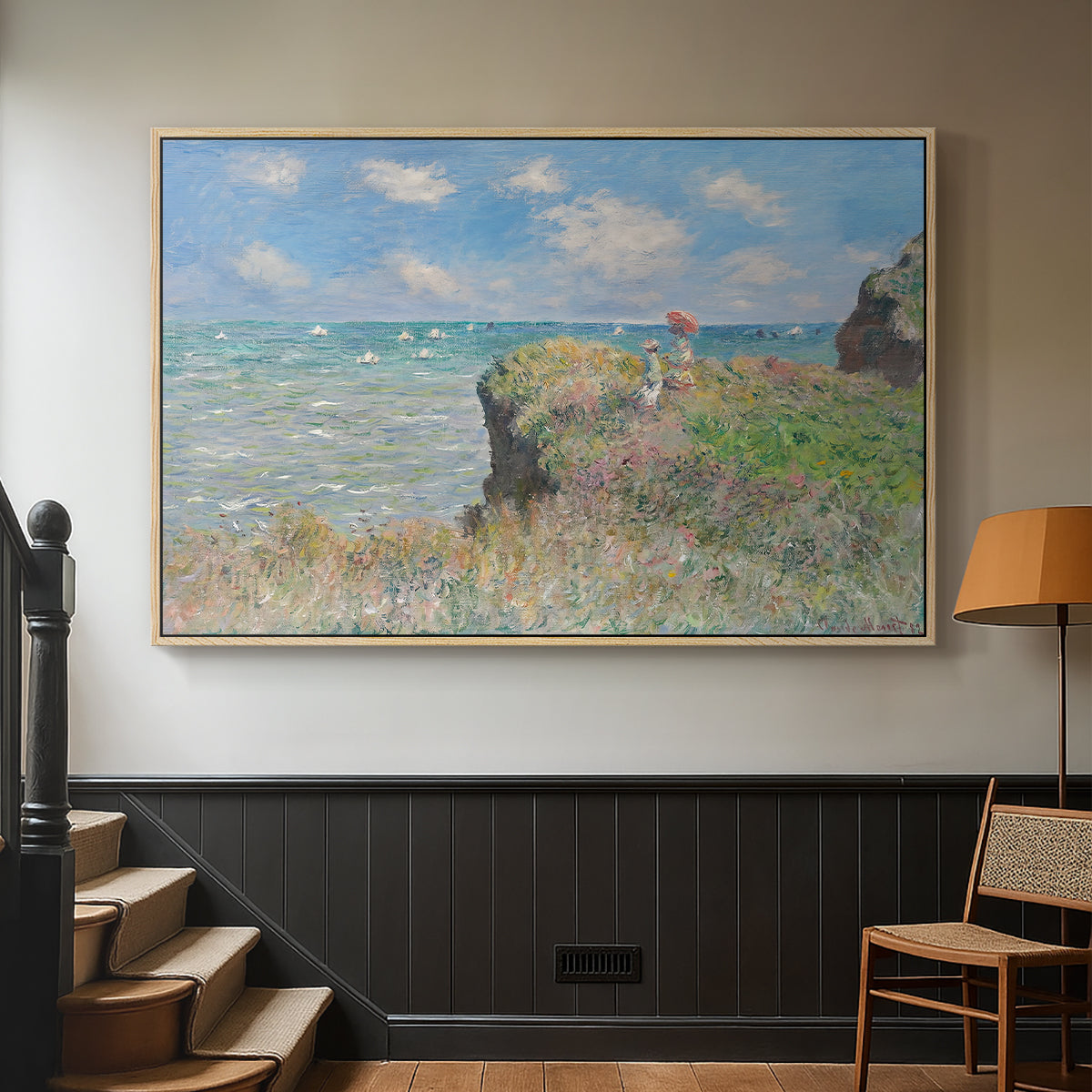 Natural wood floater framed canvas featuring an elevated shoreline path with figures and bright sky, displayed in a hallway near a staircase.